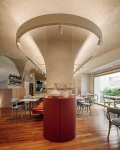 Modern restaurant interior with wooden furniture, concrete pillars, and glass elements, featuring minimalist design.