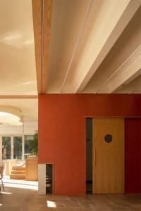 An interior space featuring modern decor, including a red wall, wooden elements, and a corridor leading to a bathroom.