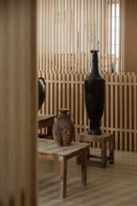 Decorative ceramic vases placed on wooden stools and tables in a room with wooden slat walls.