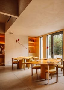 A modern, minimalist restaurant interior with wooden tables, yellow chairs, and red accents.