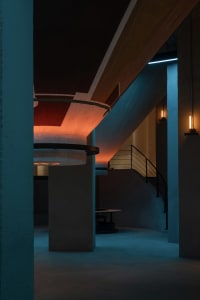A modern, minimalist interior design featuring exposed concrete walls and floors, with a spiral staircase and ambient lightin