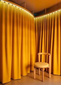 A minimalist interior with yellow curtains and a wood chair.
