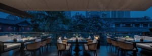 A modern restaurant dining area with wooden accents, glass tables, and metal chairs.