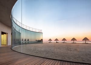 A minimalist beach house with a glass facade reflecting the sunset sky.
