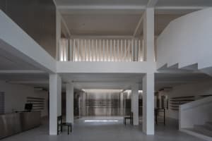A minimalist industrial storefront with concrete walls and floors, white columns, and a mezzanine level with metal railings.