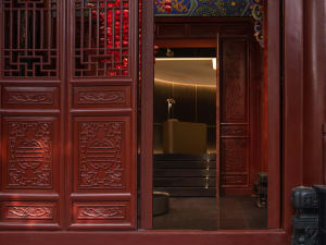 A red wooden door with intricate carvings leading to a warmly lit interior space.