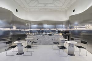 A minimalist coffee shop with metallic surfaces and sleek marble tables and chairs.