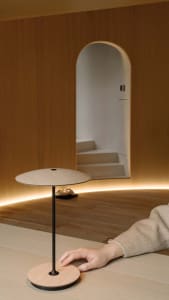 A minimalist wooden lamp with a black stand on a wooden surface in a cozy interior setting with warm lighting.