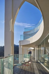 Modern residential balcony featuring glass railings and concrete pillars, set against a clear blue sky.