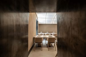 An empty, minimalist restaurant dining room with concrete walls, wooden furniture, and a skylight.