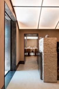 A modern minimalist restaurant corridor featuring stone, concrete, and metal elements.