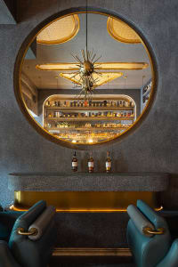 Modern industrial restaurant bar interior with concrete walls, brass accents, and circular window showcasing a well-stocked b
