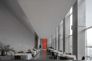 Modern restaurant with concrete walls, glass columns, and white tables and chairs.