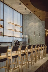 Modern restaurant interior with wooden bar counter and black leather stools