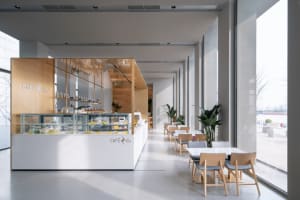 A minimalist cafe interior featuring a modern white countertop with wooden accents and glass display cases.