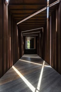 A dark, wooden and concrete corridor featuring geometric lighting patterns.