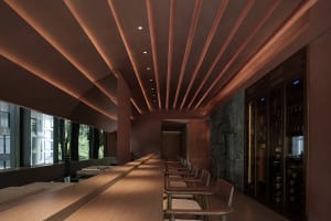 A sleek, modern restaurant bar with wooden seating and stone walls.