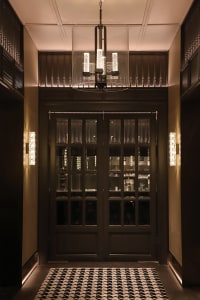 Modern entrance lobby featuring glass doors with a sleek steel frame, illuminated by contemporary lighting fixtures and a pat