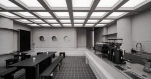 A modern coffee shop interior featuring concrete walls, glass windows, and industrial-style seating
