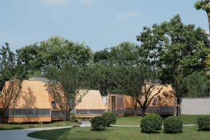 Several wooden huts arranged on a grassy area surrounded by trees.