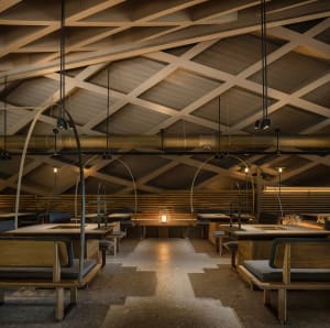 Industrial-style restaurant interior with wooden tables, arched ceiling, and hanging lights.