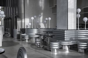 A sleek, industrial restaurant interior with metallic seating and tables.