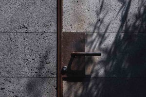 A metal door handle with a shadow cast on a concrete wall.