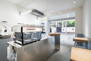 A modern coffee shop with a stainless steel counter and metal stools