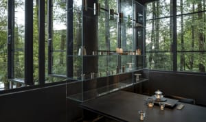A minimalist restaurant interior with glass walls and wooden accents, featuring sleek metal furniture and a large display cas