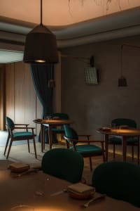 A modern restaurant interior with wooden furniture and green upholstered chairs.