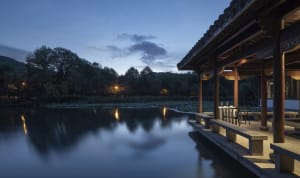 A serene waterfront retreat with stone sculptures reflecting on a tranquil pond, surrounded by lush greenery.