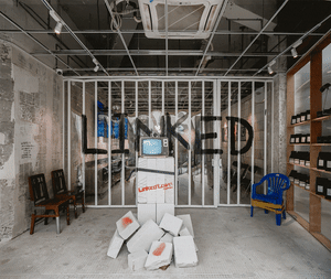 A contemporary art installation featuring found objects arranged in a geometric structure with the word 'LINKED' spelled out 