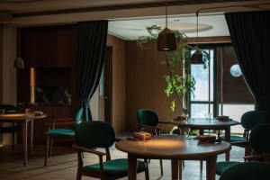 A modern restaurant interior featuring wooden tables, green fabric chairs, and glass accents.