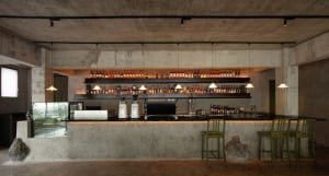 An industrial-style bar with a concrete counter and shelves filled with bottles of alcohol.