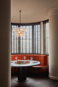 A round dining table with a lazy Susan, glasses, and plates, surrounded by a cozy orange velvet booth seating area with large