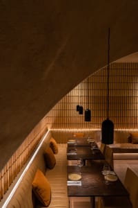 A cozy, industrial-themed restaurant interior with concrete and tiled walls, wooden tables, and plush seating.