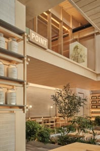 Contemporary cafe interior with wooden elements, glass partitions, and green plants.