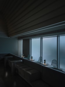 A minimalist restaurant interior featuring metallic furniture and large glass windows.