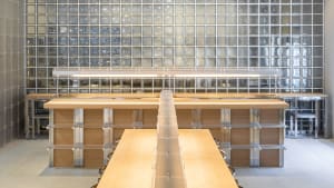 A modern workspace featuring wooden tables, glass walls, and metallic structural elements.