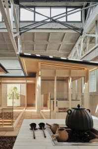 Modern minimalist tea ceremony space with wooden furniture, concrete floor, steel and glass structural elements.