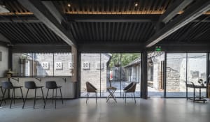 A modern industrial bar lounge with concrete and wood materials, featuring tall stools and chairs.