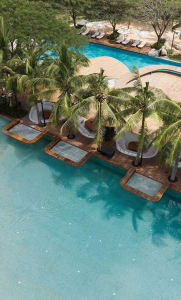 Aerial view of a resort poolside area with concrete structures and palm trees.