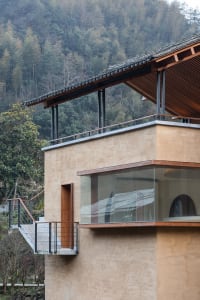 A modern house with a clay exterior features large glass windows and a traditional tiled roof.