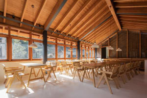 A spacious restaurant interior with wooden tables, chairs, and a high, wooden-beamed ceiling.