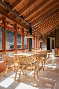 Modern restaurant interior with wooden tables and chairs, large windows, and natural light.