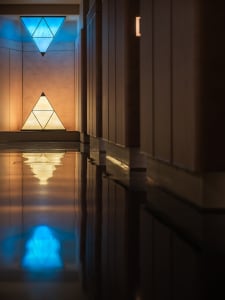 A modern swimming pool with a glass wall reflecting the blue light from a triangular light fixture.