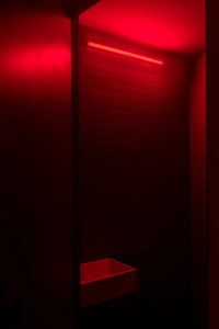 A minimalist bathroom with red lighting and ceramic tile walls and floor.