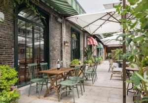 A cozy outdoor seating area with wooden furniture and greenery in a cafe setting