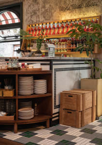 A coffee shop's retail counter featuring a wooden shelf with plates, metal bar counter, and potted plants.