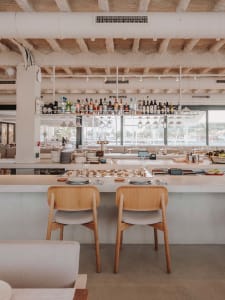 A minimalist restaurant bar with concrete walls and wooden chairs.